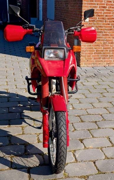 Ein rotes Motorrad ist auf einem gepflasterten Gehweg vor einem Backsteingebäude geparkt.