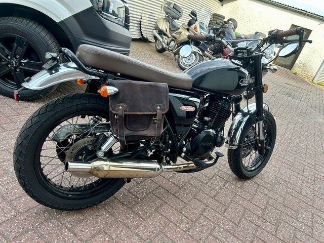 Schwarzes Oldtimer-Motorrad mit brauner Ledersatteltasche auf gepflastertem Pflaster.