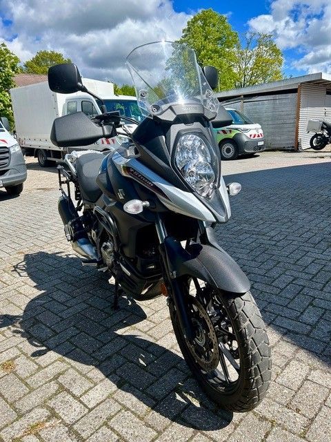 Schwarzes Tourenmotorrad mit Windschutzscheibe, geparkt auf einem Kopfsteinpflasterparkplatz im hellen Sonnenlicht.
