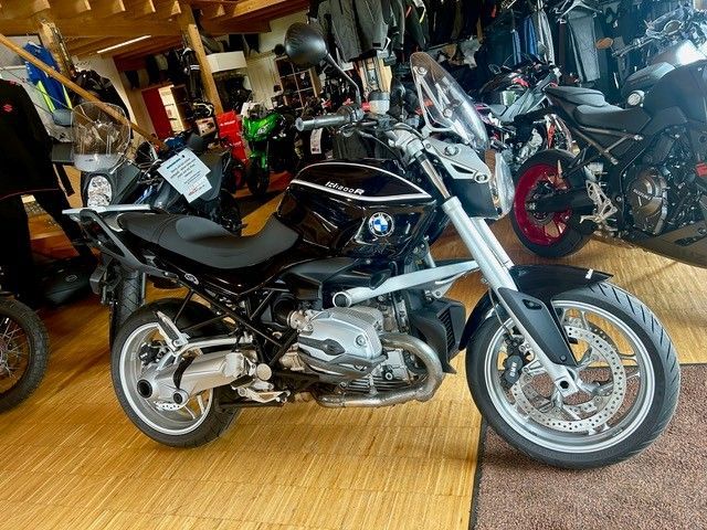Schwarzes Motorrad in einem Ausstellungsraum, umgeben von mehreren anderen Motorrädern im Innenbereich.