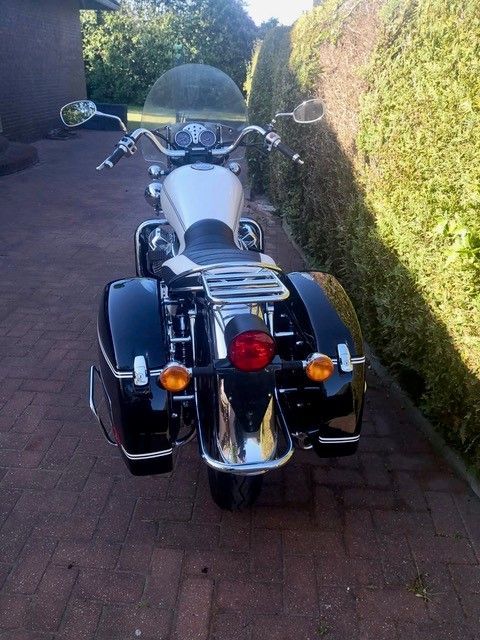 Schwarz-weißes Motorrad mit Satteltaschen, Chrom-Akzenten und getönter Windschutzscheibe, auf Ziegelstein geparkt.