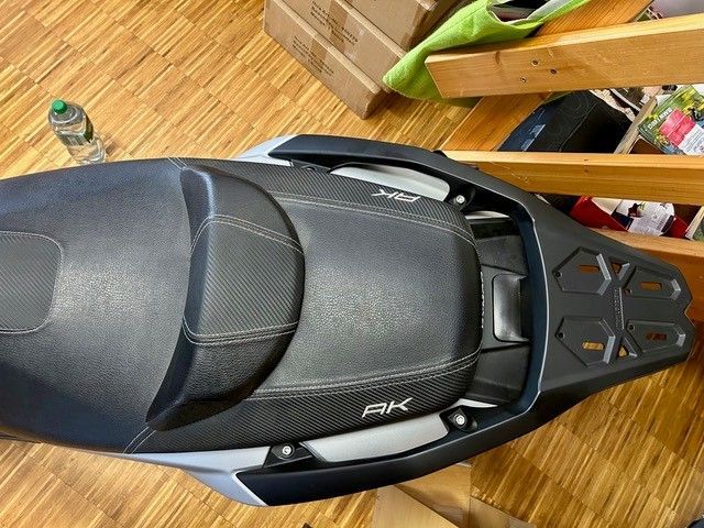 Schwarzer Motorradsitz, von oben betrachtet, auf einem Holzboden mit grünen und orangen Akzenten.