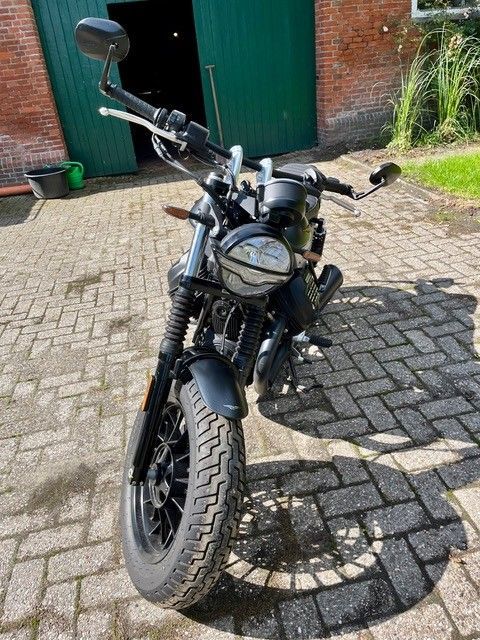 Schwarzes Motorrad, tagsüber auf Pflastersteinen vor einer grünen Tür geparkt.