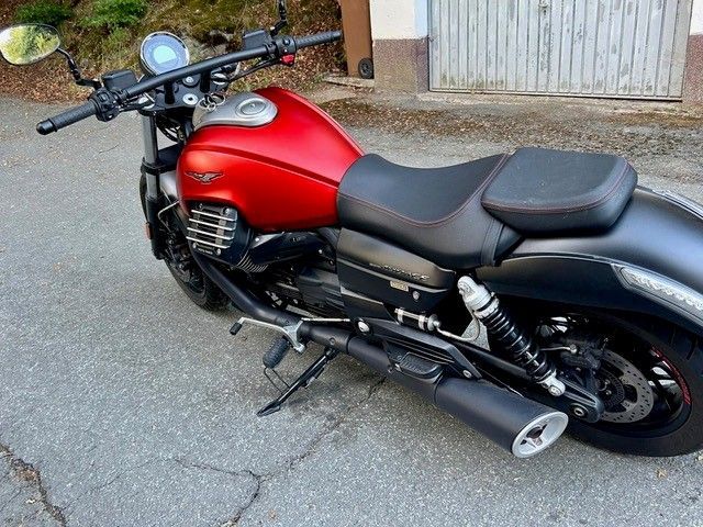 Ein rot-schwarzes Motorrad parkt auf dem Bürgersteig neben einem Garagentor.
