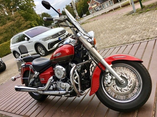 Ein rotes Motorrad ist auf einem Holzdeck neben einem weißen SUV geparkt.