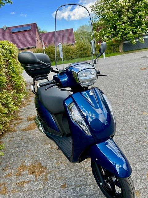 Ein blauer Roller mit Windschutzscheibe ist auf einer gepflasterten Straße geparkt