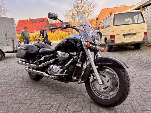 Auf einem Parkplatz steht neben einem Lieferwagen ein schwarzes Motorrad.
