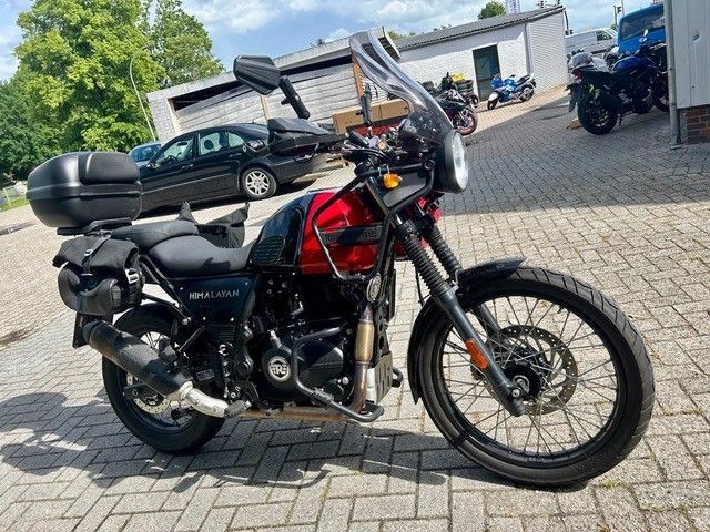 Ein schwarz-rotes Motorrad parkte auf einer gepflasterten Auffahrt in der Nähe von Häusern und anderen Fahrzeugen.