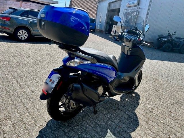 Ein blauer Motorroller mit einem Helm auf der Rückseite steht auf einem Parkplatz.