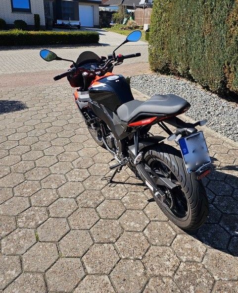 Auf einer gepflasterten Auffahrt ist ein schwarz-oranges Motorrad geparkt.
