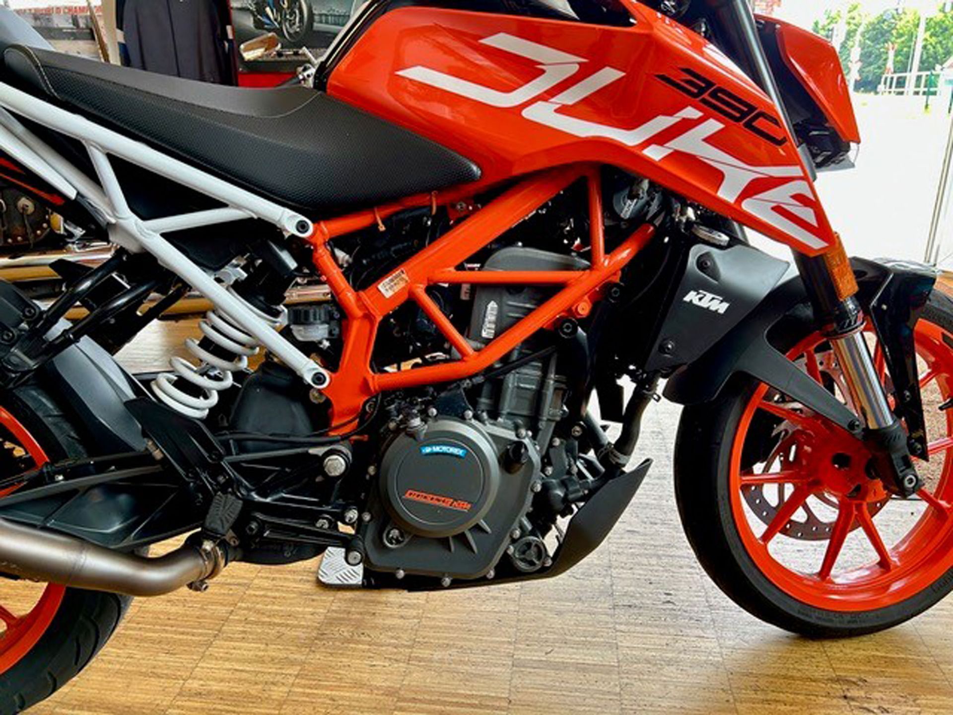 Orangefarbenes Motorrad KTM 390 Duke. Das Motorrad hat einen weißen Rahmen, einen schwarzen Motor und orangefarbene Räder und steht im Innenbereich.