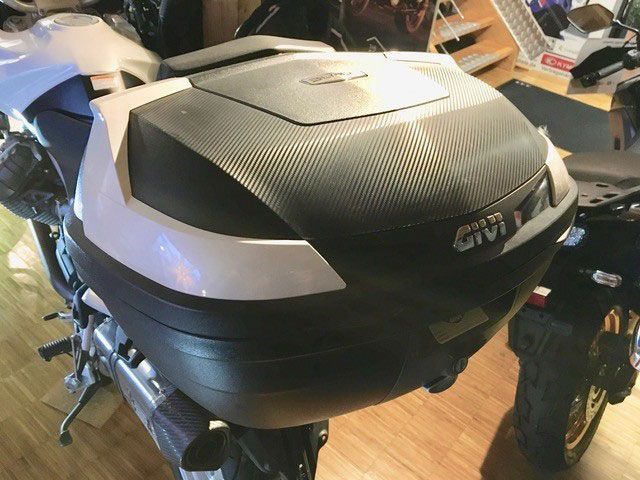 Ein Motorrad mit einem Givi-Topcase ist auf einem Holzboden geparkt.