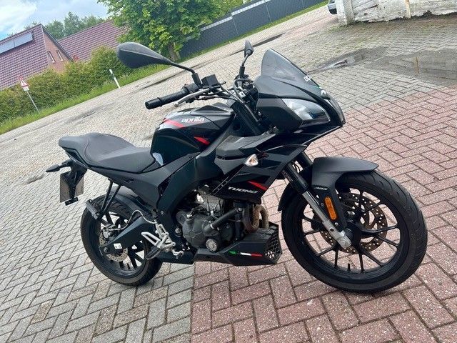 Schwarzes Sportmotorrad parkt auf einer gepflasterten Auffahrt neben einer grasbewachsenen Wohnstraße.