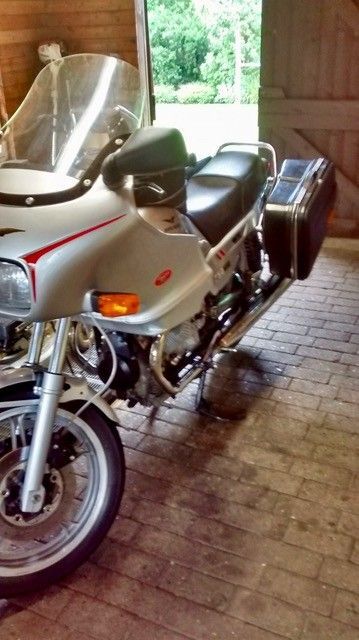 Silbernes Tourenmotorrad, abgestellt auf Ziegelboden in einer Garage, mit Windschutzscheibe und Seitenkoffern