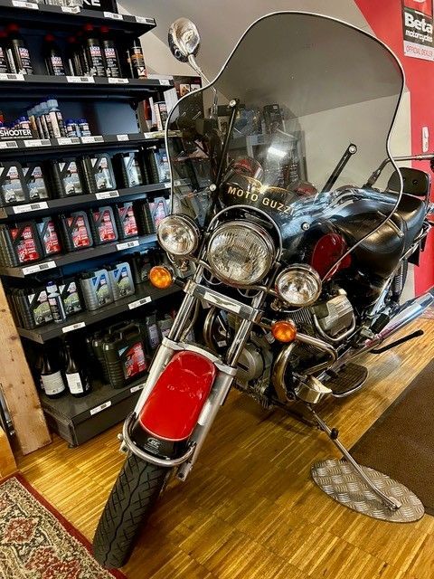 Rotes Oldtimer-Tourenmotorrad in einem Geschäft, mit Chromdetails und hoher Windschutzscheibe.