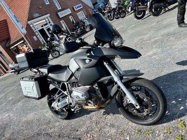 Schwarz-silbernes BMW-Motorrad mit Gepäck im Freien in der Nähe eines Gebäudes geparkt; andere Motorräder sichtbar.