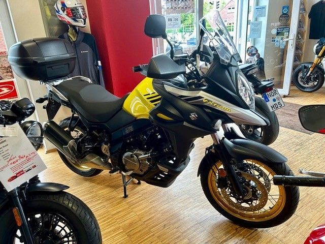 Schwarzes Tourenmotorrad mit goldenen Felgen in einem Ausstellungsraum, daneben teilweise ein schwarzer Roller zu sehen.