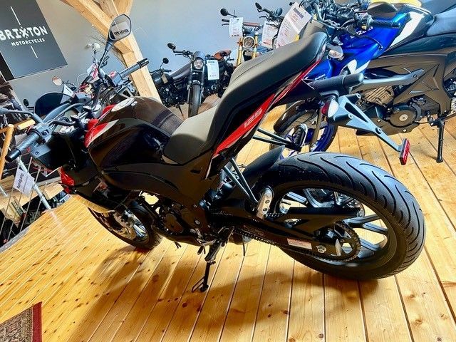 Schwarzes Sportmotorrad auf Holzboden in einem Ausstellungsraum, im Hintergrund weitere Motorräder.