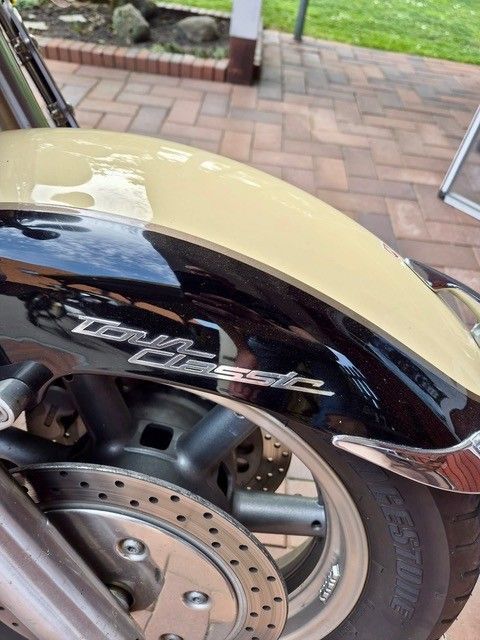 Nahaufnahme eines Motorradhinterrads und eines verchromten Auspuffs unter einem cremefarbenen und schwarzen Schutzblech im Freien