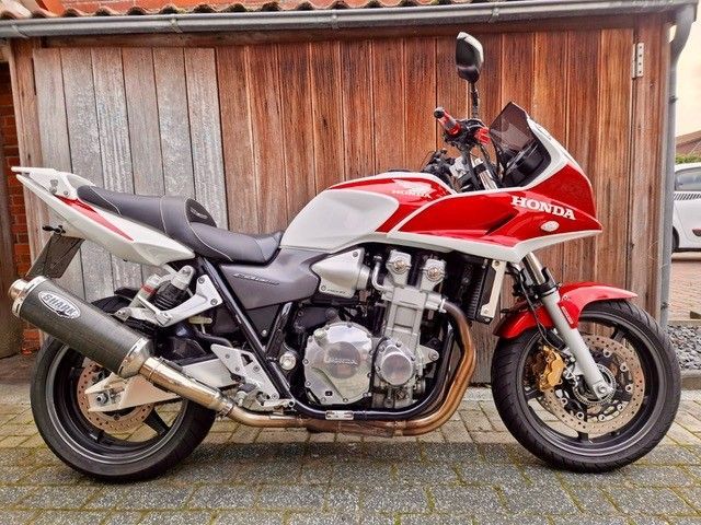 Rot-weißes Honda-Motorrad, das vor einem Holzgebäude geparkt ist.
