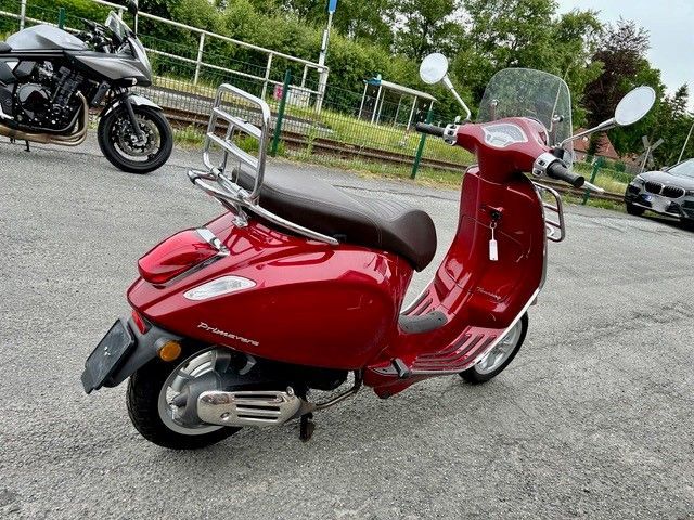 Ein roter Motorroller steht auf einem Parkplatz neben einem Motorrad.
