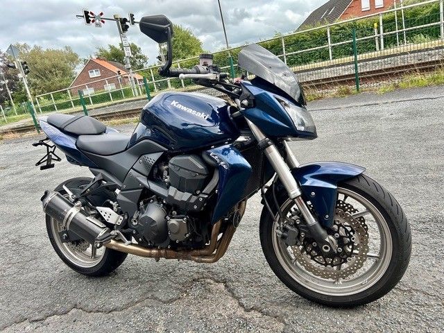 Ein blaues Sportmotorrad parkt auf einem rissigen Asphaltparkplatz unter einem bewölkten Himmel.
