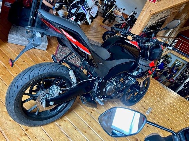 Schwarzes Sportmotorrad in einem Innenraum, von hinten links gesehen, mit einem Spiegel auf dem Boden davor.