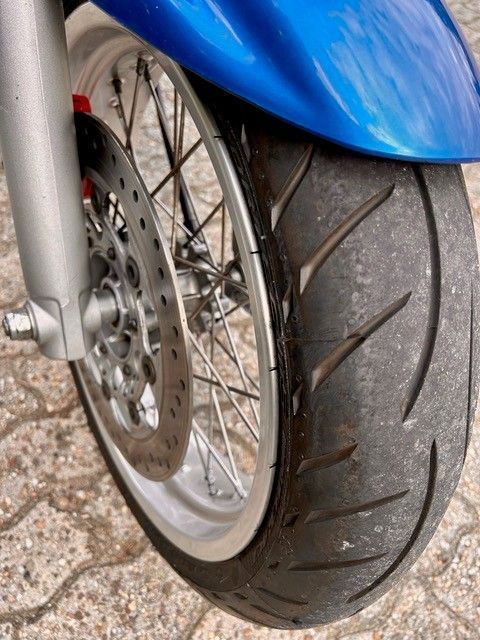 Blauer Motorrad-Vorderreifen mit abgefahrenem Profil und silberner Felge.