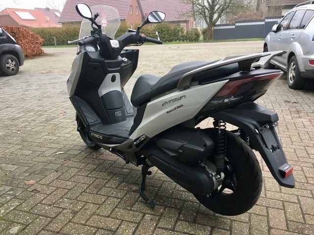 Auf einer gepflasterten Auffahrt ist neben einem Auto ein Motorroller geparkt.