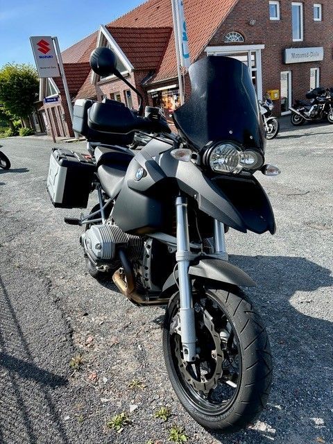 Graues BMW-Motorrad vor einem Gebäude mit einem Suzuki-Schild geparkt; sonniger Tag.