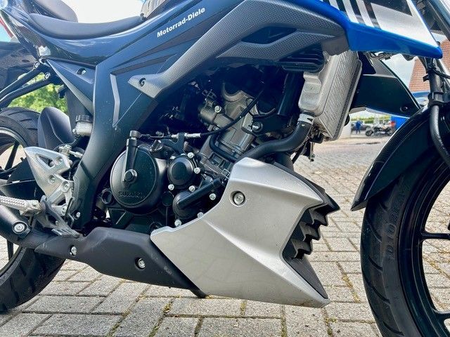 Blau-schwarzes Motorrad auf gepflasterter Fläche geparkt, Nahaufnahme von Motor und Vorderrad