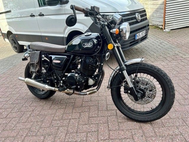Ein schwarzes Cruiser-Motorrad parkt auf dem gepflasterten Gehweg neben einem silbernen Lieferwagen.
