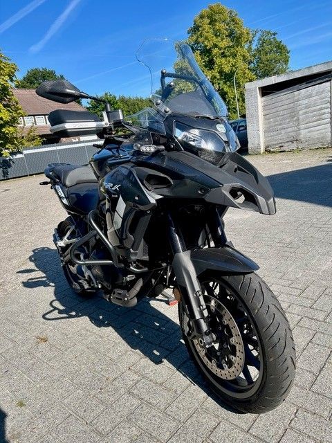Schwarzes Sporttouring-Motorrad parkt auf einer sonnigen Auffahrt neben einer Garage und Bäumen.