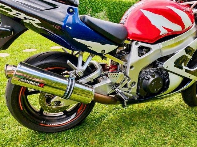 Sportmotorrad mit roter, blauer und weißer Farbe. Chromauspuffrohr liegt auf grünem Gras.