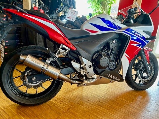 Ein rot-weiß-blaues Honda-Sportmotorrad steht in einem Innenraum auf einem Holzboden.