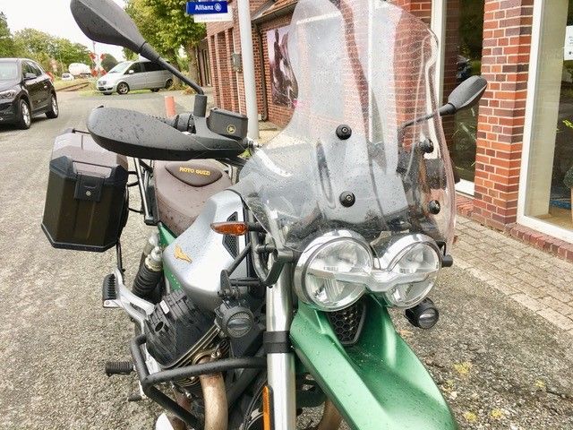 Ein grünes Motorrad mit Windschutzscheibe ist vor einem Backsteingebäude geparkt.