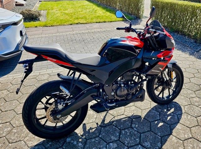 Ein rot-schwarzes Motorrad ist neben einem silbernen Auto geparkt.