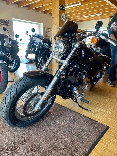 Ein schwarzes Cruiser-Motorrad ist in einem Ausstellungsraum ausgestellt, im Hintergrund sind weitere Motorräder zu sehen.