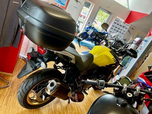 Motorräder parkten in einer Halle, darunter ein gelbes Motorrad mit Topcase im Vordergrund.