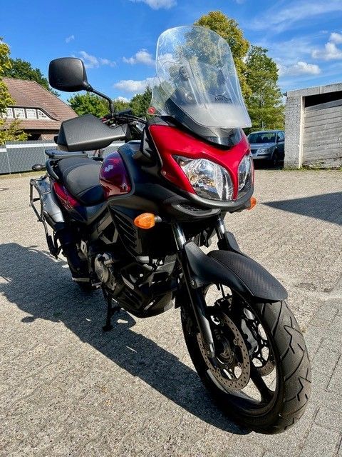 Ein rot-schwarzes Motorrad mit hoher Windschutzscheibe parkt in einer sonnigen Wohnstraße.