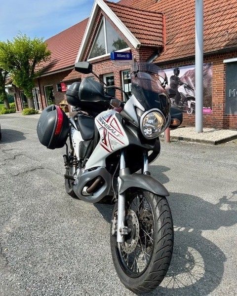 Weißes und graues Motorrad, das auf einem gepflasterten Platz vor einem Gebäude geparkt ist.
