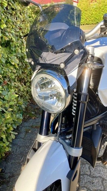 Weißes Motorrad mit rundem Scheinwerfer, kleiner Windschutzscheibe und Vordergabel.