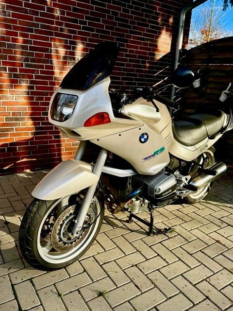 Auf einer gepflasterten Auffahrt vor einem Backsteingebäude ist ein Motorrad geparkt.