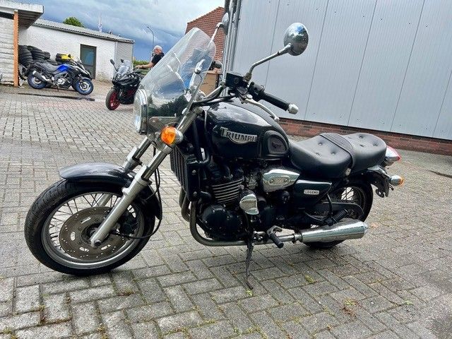 Schwarzes Cruiser-Motorrad mit Windschutzscheibe parkt auf einem gepflasterten Parkplatz in der Nähe eines Gebäudes und einer Garage.