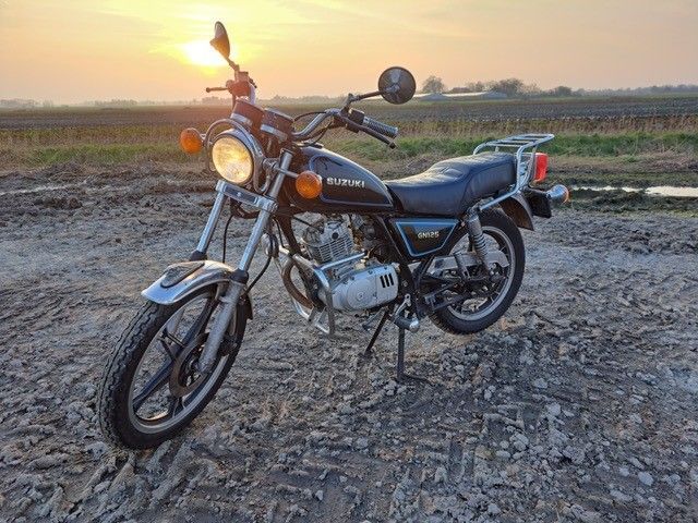 Bei Sonnenuntergang ist ein schwarzes Motorrad auf einem Feld geparkt.