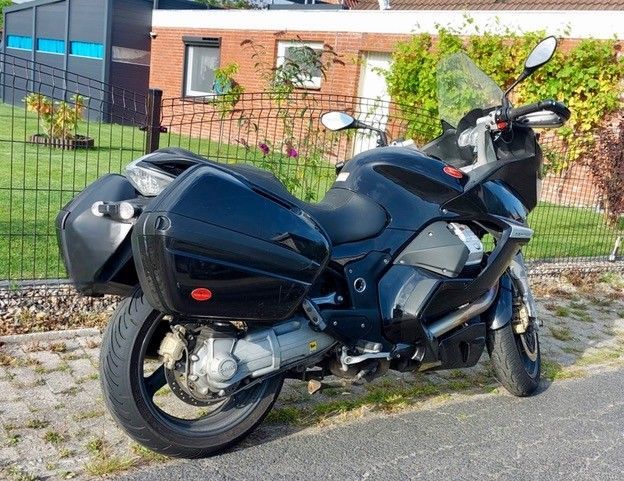 Schwarzes Motorrad mit Seitenkoffern auf einer Straße vor einem Zaun und einem Haus geparkt.