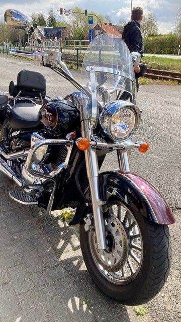 Ein Mann steht neben einem am Straßenrand geparkten Motorrad.