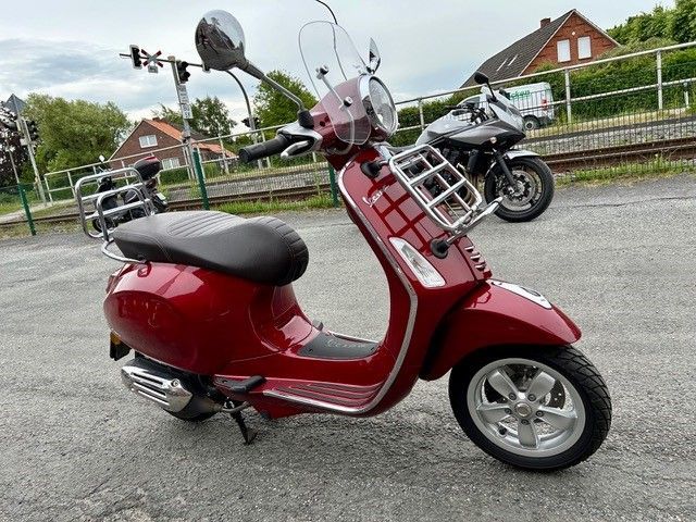 Ein roter Motorroller steht auf einem Parkplatz neben einem Motorrad.