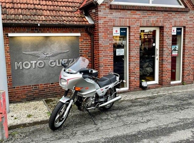 Ein silbernes Motorrad parkte vor einem gemauerten Moto-Guzzi-Laden mit rotem Ziegeldach.