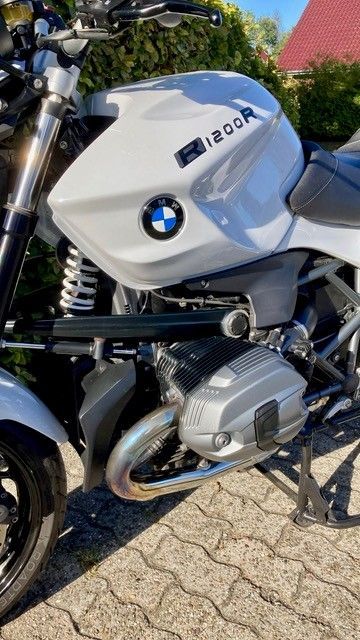 Weißes Motorrad BMW R1200R, geparkt auf einer Ziegelfläche, mit silbernem Motor und schwarzen Akzenten, im Freien.